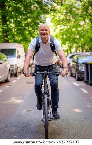 Mid aged man using a bicycle on the street. Commuter man going to work and wearing casual clothes. Full length. 
