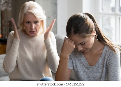 Mid aged mother sit on couch scold grown up daughter, angry mum tell complaints lecturing teen adult child feeling stressed, misunderstandings, generational gap, difficulties in relationships concept
