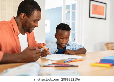 Mid Black Father Helping His Son With Homework. African American Boy Studying With Dad At Home. Cute Little Child Doing Homework And Studying With The Help Of His Mature Dad.