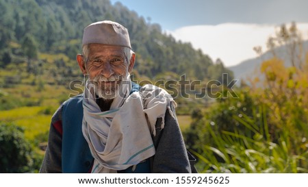 Mid Close up of an old village Indian man smiling at the camera in front of a beautiful valley with expression of contentment and peace enjoying perfect health in Uttarakhand, India 