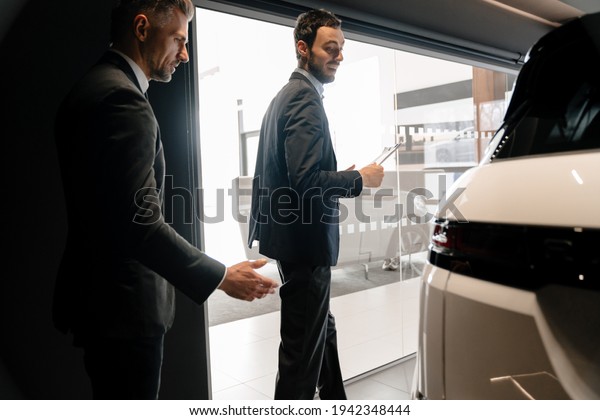 Mid pleased manager showing car to mature\
customer in showroom