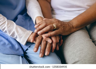Mid section of Asian female doctor holding hand of senior African American patient at retirement home