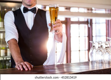 Mid section of bartender standing at bar counter offering a glass of beer
