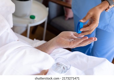 Mid section of biracial female health worker giving medical pills to caucasian senior man on the bed. Medical care and retirement senior lifestyle concept - Powered by Shutterstock