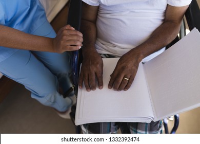 Mid section of blind senior African American man reading a braille at home. African American female doctor is helping with reading. - Powered by Shutterstock