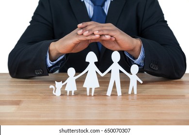 Mid section of businessman protecting paper cut out family, house and car with hands - Powered by Shutterstock