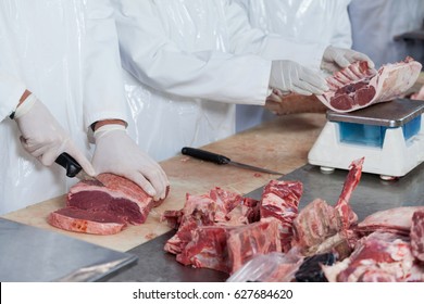 Mid section of butchers cutting meat and checking the weight of meat at meat factory - Powered by Shutterstock