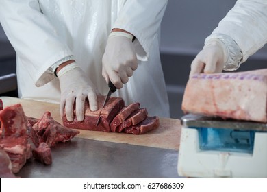 Mid section of butchers cutting meat and checking the weight of meat at meat factory - Powered by Shutterstock