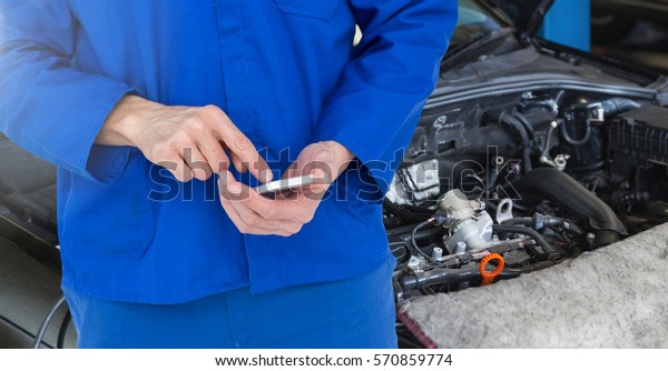 Mid\
section of car mechanic using mobile phone at\
garage