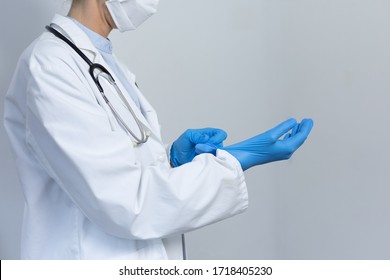 Mid Section Of A Caucasian Female Healthcare Worker Wearing A Lab Coat And Face Mask Against Coronavirus, Covid 19, Putting On Surgical Gloves.