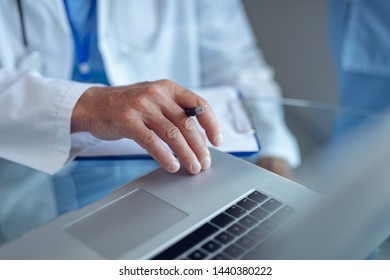 Mid section of Caucasian male doctor sitting with laptop in hospital - Shutterstock ID 1440380222