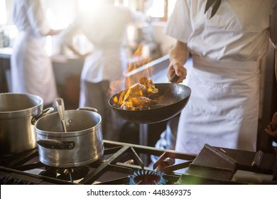Mid section of chef tossing stir fry over large flame in commercial kitchen - Powered by Shutterstock
