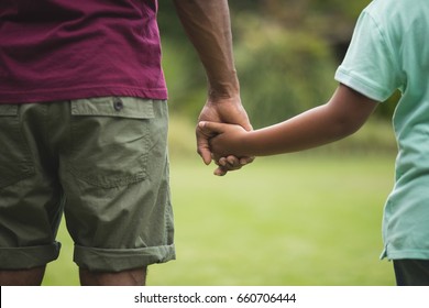 Mid section of father and son holding hands at park