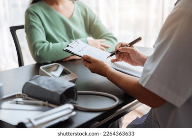 Mid section of female doctor writes prescription to patient at worktable. - Powered by Shutterstock