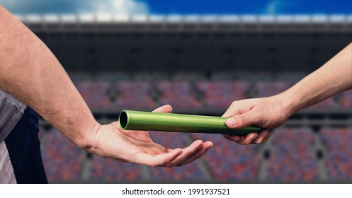 Mid section of hand passing a baton against sports stadium in background. sports competition and tournament concept