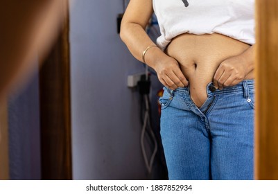 Mid Section Of An Indian Woman With Belly Fat Wearing Blue Jeans In Front Of Mirror