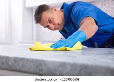 Mid Section Of A Male Janitor Cleaning Dirty Kitchen Counter With Spray Bottle And Napkin