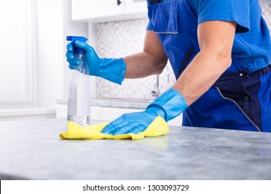 Mid Section Of A Male Janitor Cleaning Dirty Kitchen Counter With Spray Bottle And Napkin