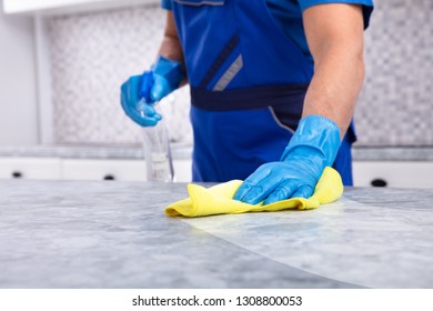 Mid Section Of A Male Janitor Cleaning Dirty Kitchen Counter With Spray Bottle And Napkin