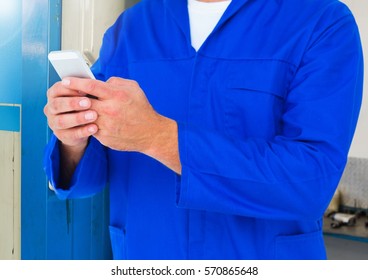 Mid section of mechanic using a mobilephone at workshop