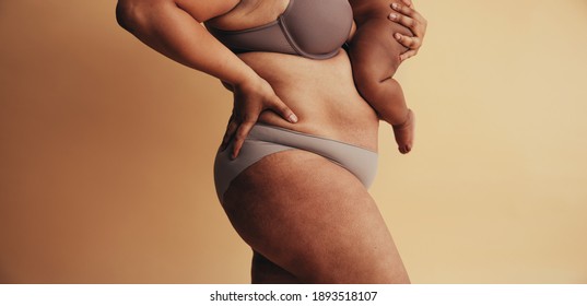 Mid section of plus size woman with baby. Body positive woman postpartum. Mother with visible postpartum body marks with baby.