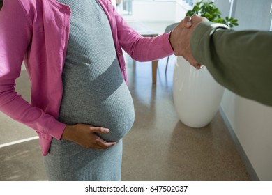 Mid section of pregnant woman shaking hand with colleague in office - Powered by Shutterstock