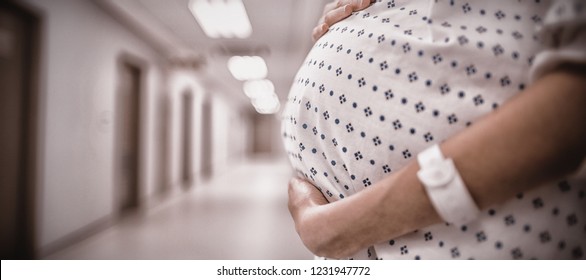 Mid section of pregnant woman standing in corridor of hospital