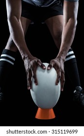 Mid Section Of Rugby Player Keeping Ball On Kicking Tee Against Black Background