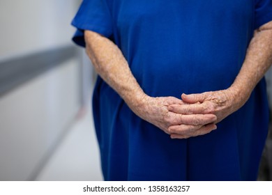 Mid section of a senior Caucasian female patient standing in hospital clinic with her hands joined