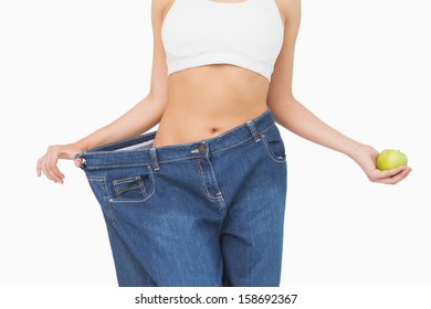 Mid Section Of Slim Woman Wearing Too Big Jeans Holding An Apple On White Background