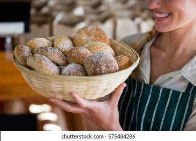 Mid section of smiling female staff holding basket of sesame breads at bread counter in supermarket - Powered by Shutterstock