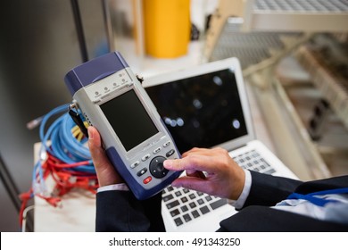 Mid section of technician using digital cable analyzer in server room