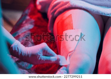 Mid section of therapist waxing woman's leg at spa center