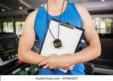 Mid section of trainer standing in gym with clipboard and stopwatch - Powered by Shutterstock