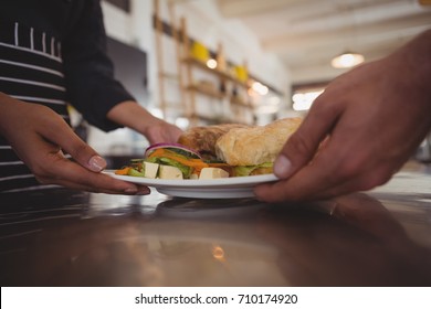 Mid Section Of Waitress Giving Plate With Food To Coworker At Counter In Cafe