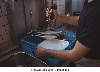 Mid Section Of Washing Plates At Sink In Commercial Kitchen