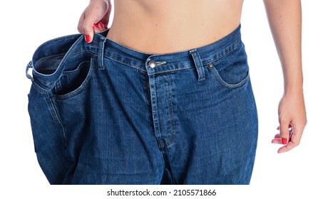 mid section of a woman with belly fat holding her blue jeans. Girl with big jeans isolated on white background. Woman shows her weight loss. Healthy lifestyle concept