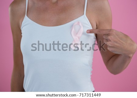 Mid section of woman gesturing on Breast Cancer Awareness ribbon while standing against pink background