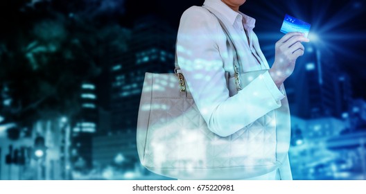 Mid Section Of Woman Holding Credit Card Against Illuminated Roads By Building In City