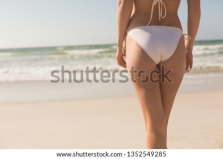 Mid section of young Caucasian woman in bikini standing on beach. It is sunny day