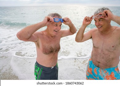 Mid shot of a mature man with a friend in swimming trunks adjusting goggles on the beach. - Powered by Shutterstock