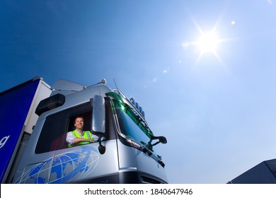 A Mid Shot With A Truck Driver Looking Outside Through The Open Window Of A Semi Truck On A Bright Sunny Day