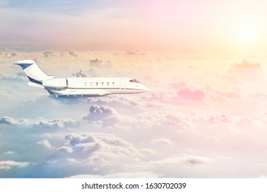 Mid Size Modern Vip Private Jet Flying High In Sky Over Evening Fluffy Curly Clouds At Warm Colorful Sunset Time. Luxury Small Corporate Business Aircraft Trip . Travel Beautiful Skyline Background