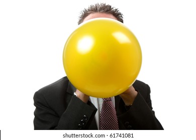 A mid thirties business man blowing up a yellow balloon.  Facing camera.   Studio isolated on a white background.