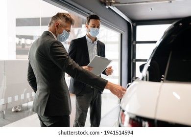 Mid White Manager In Face Mask Showing Car To Customer In Showroom