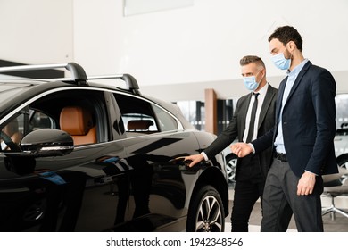 Mid White Manager In Face Mask Showing Car To Customer In Showroom