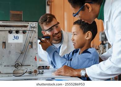 A mid-adult Caucasian male and black female scientist teach robotics to a young boy, adjusting a control panel in a laboratory setting, clad in lab coats. - Powered by Shutterstock