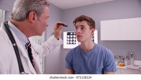Mid-aged doctor examining eyes of young adult male patient.