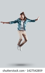 Mid-air fun. Full length of handsome young man keeping arms outstretched while hovering against grey background