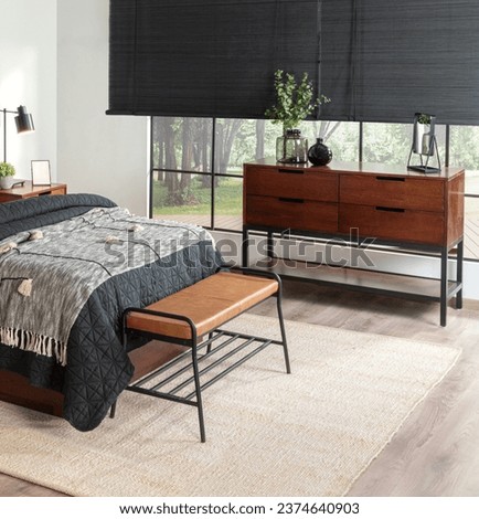Mid-Century Modern Bedroom: Charcoal Quilted Bedspread on Cozy Bed, Sleek Walnut Wood Sideboard with Decorative Green Plant, Brown Leather Bench on Black Metal Frame, Set Against a Bright Window.